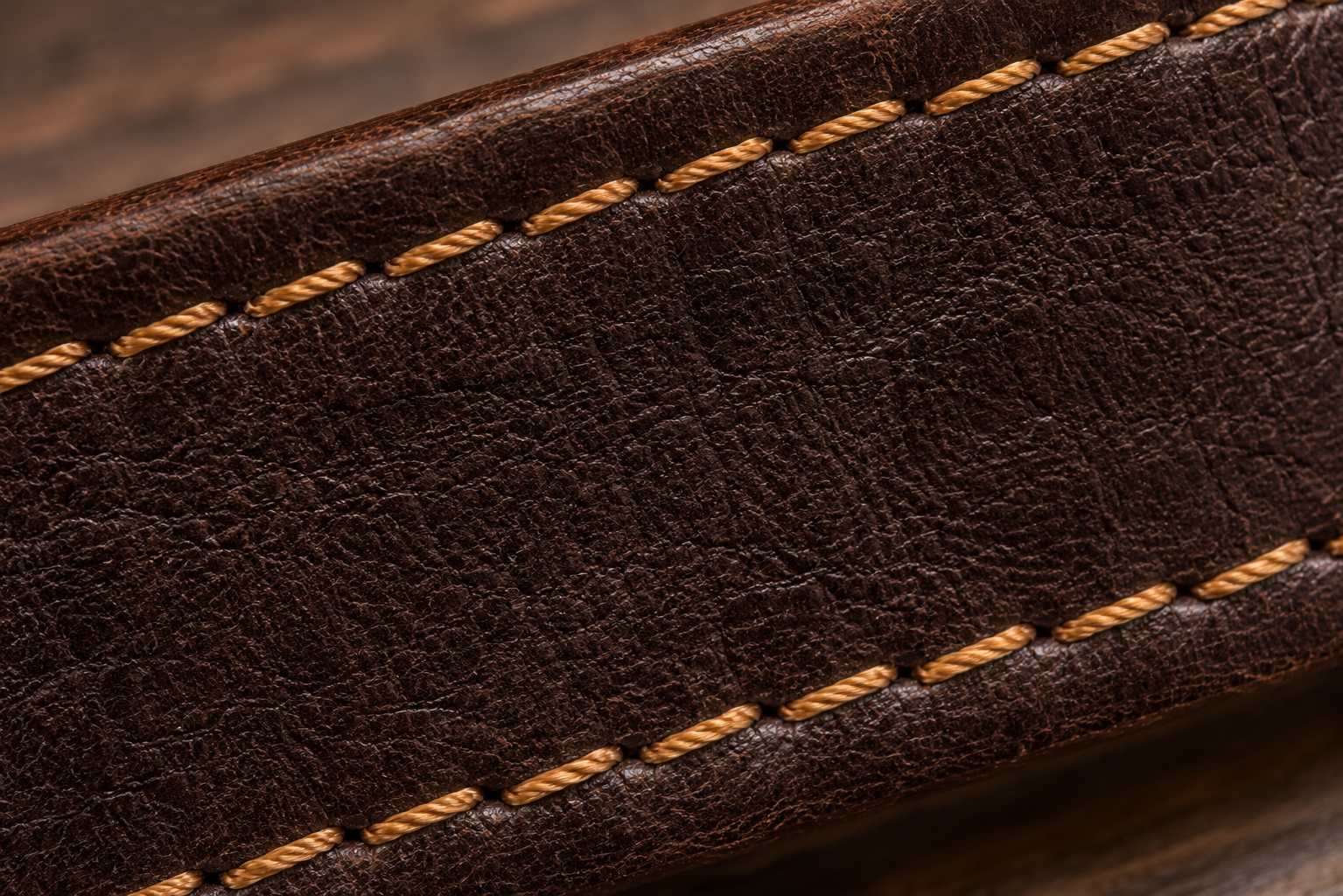 Close-up view of a brown leather belt with yellow stitching on a wooden surface