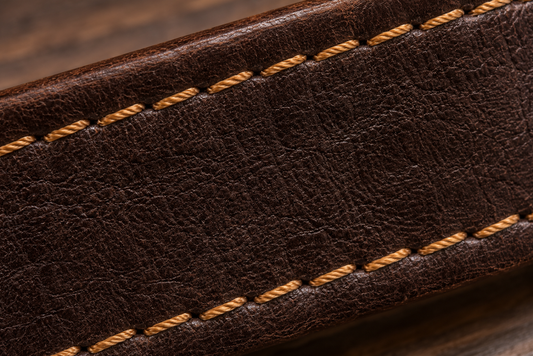 Close-up view of a brown leather belt with yellow stitching on a wooden surface